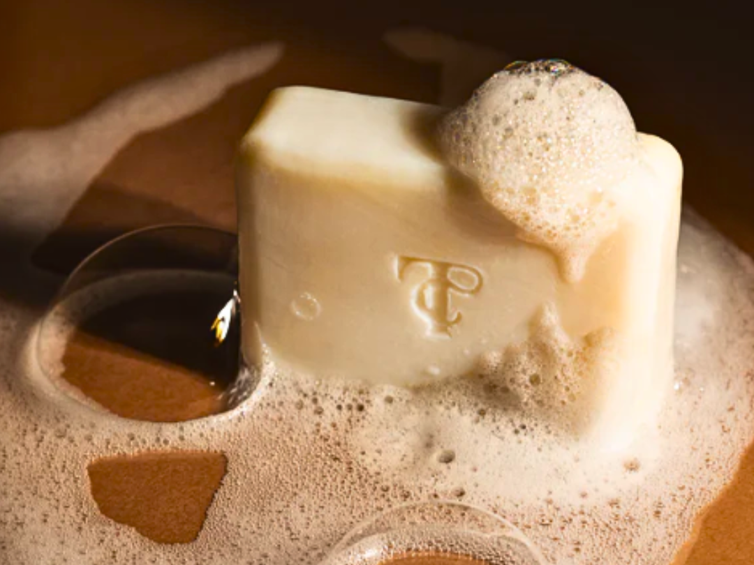 Herbal tallow soap bar with foamy lather in a soap dish (close-up)